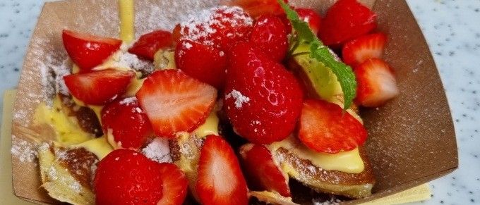 Eine braune Box mit French Toast, garniert mit frischen Erdbeeren und Puderzucker. Eine Minzblatt und ein Holzstäbchen sind auf der Seite.