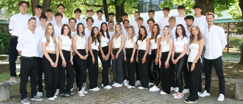 Eine Gruppe junger Erwachsener in weißer und schwarzer Kleidung, die für ein Foto in einem Park posiert. Sie stehen auf einem Ziegelboden mit Bäumen im Hintergrund.