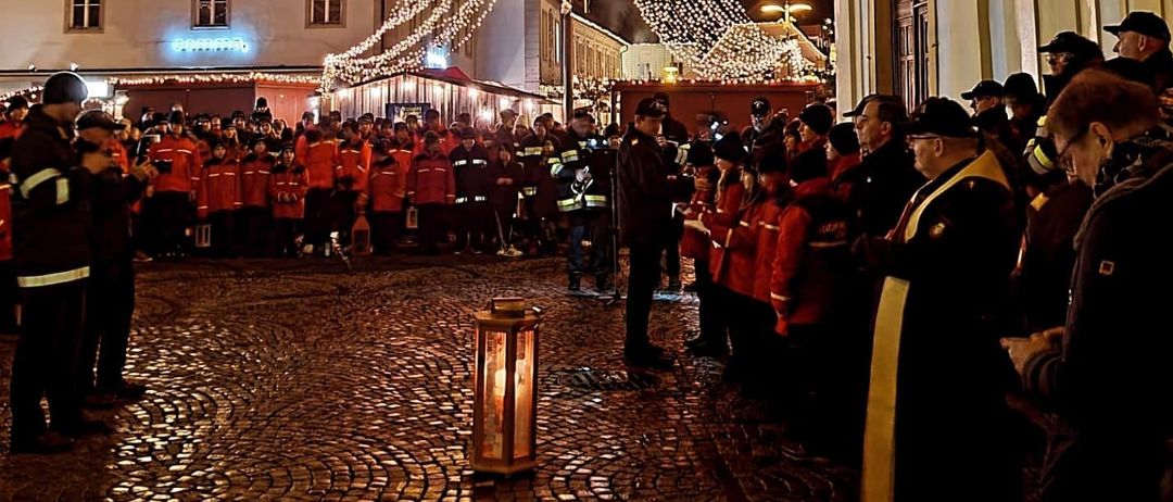 Eine Nachtszene mit Menschen in roten Uniformen vor einem Gebäude, möglicherweise einer Kirche, mit dekorativen Lichtern.