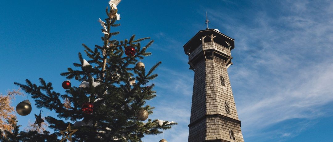 Ein Weihnachtsbaum mit Dekoration steht vor einem Turm gegen einen blauen Himmel mit leichten Wolken.