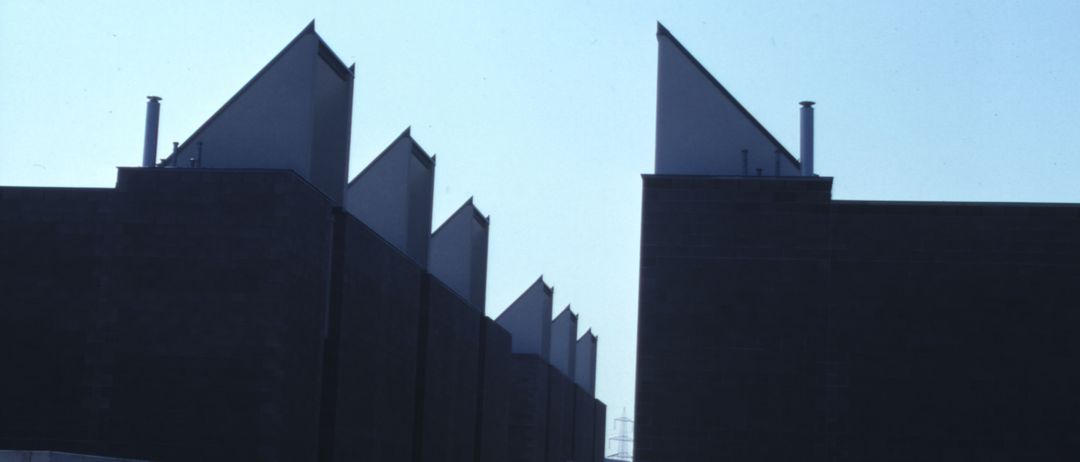 Eine Reihe hoher, rechteckiger Gebäude mit dreieckigen Dächern. Die Gebäude sind im Bau, mit sichtbaren Betonwänden.