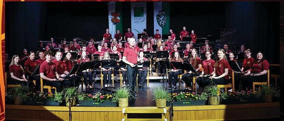 Ein Plakat für ein Sommerkonzert des Jugendblasorchesters der Musikschule Hartberg. Das Orchester ist auf der Bühne, Musiker spielen Instrumente.
