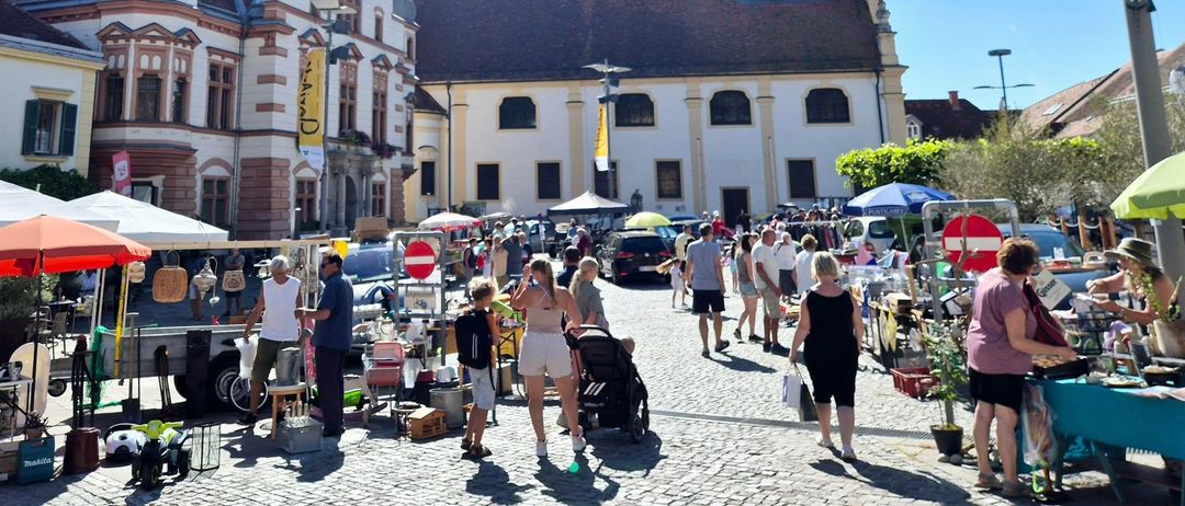Ein sonniger Tag mit einem Markt vor einer alten Kirche. Verschiedene Stände und Menschen, die herumlaufen.