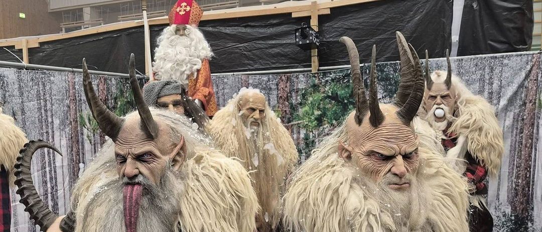 Eine Gruppe von Personen, die in aufwendigen, gehörnten Kostümen gekleidet sind. Sie stehen vor einer Kulisse mit Logos und Bannern. Die Umgebung scheint ein Indoor-Event zu sein, möglicherweise eine Cosplay-Versammlung oder eine thematische Party.