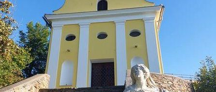 A yellow and white church with a tower and a statue of a woman on the steps.