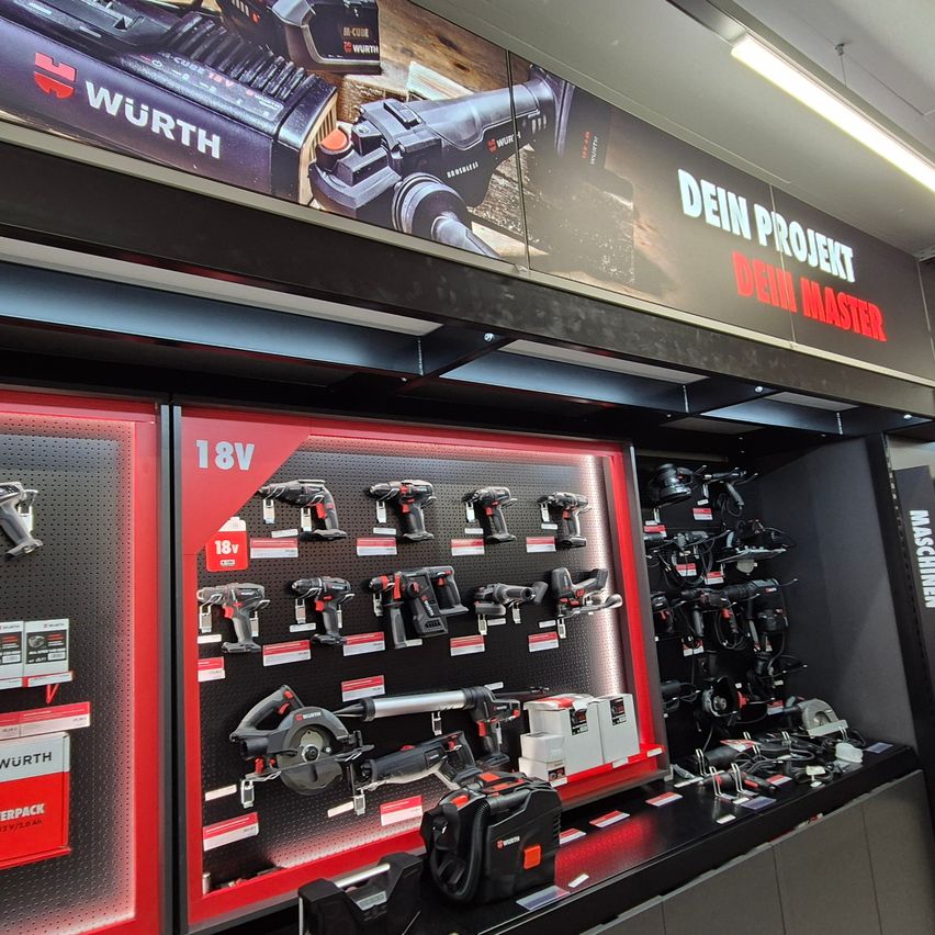 Geschäftsinnenraum mit roter Anzeige von 18V-Elektrowerkzeugen. Über der Anzeige befindet sich ein großes Schild mit den Worten 'Dein Projekt Dein Master'.