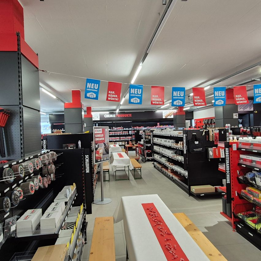 Ein Innengeschäft mit Regalen, die verschiedene Produkte präsentieren. Rote und blaue Banner hängen von der Decke, und ein rot-weißes Banner liegt auf dem Boden.