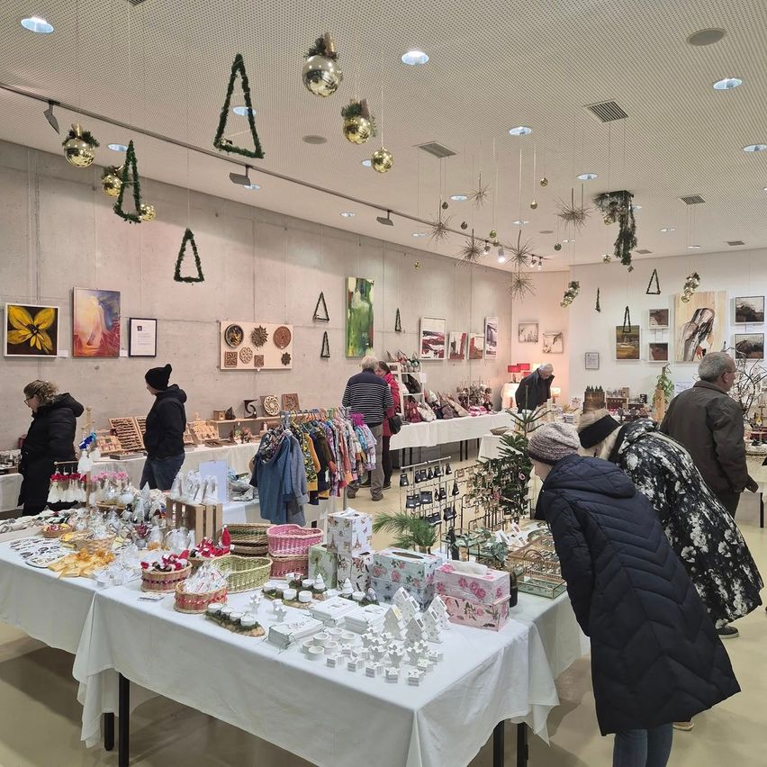 An indoor market with several tables displaying various items. People are browsing the products. There are decorations hanging from the ceiling.