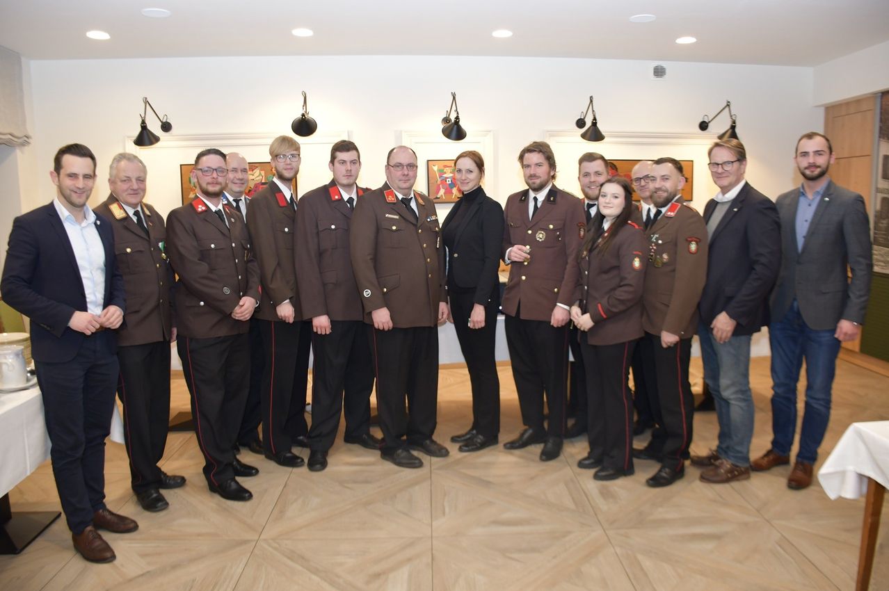 A group of individuals dressed in military uniforms stands in a room with tiled floors. They are possibly posing for a photo. Behind them are walls with hanging lamps and picture frames.