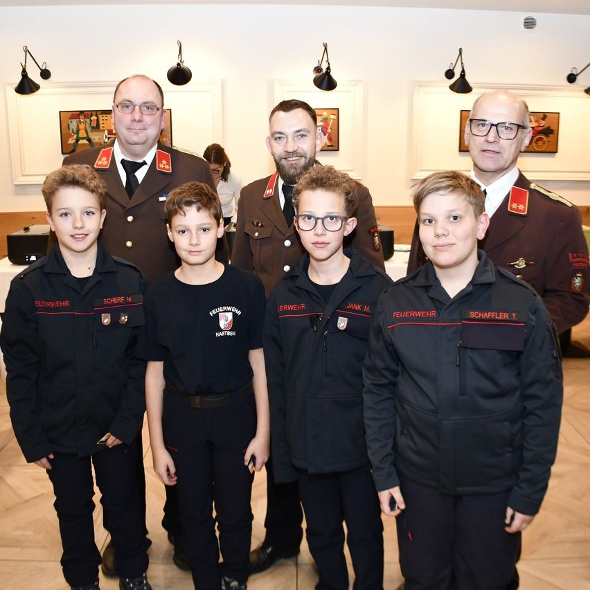 Five young boys in black uniforms with red trim stand together with three men in military uniforms. They are all smiling for a photo.