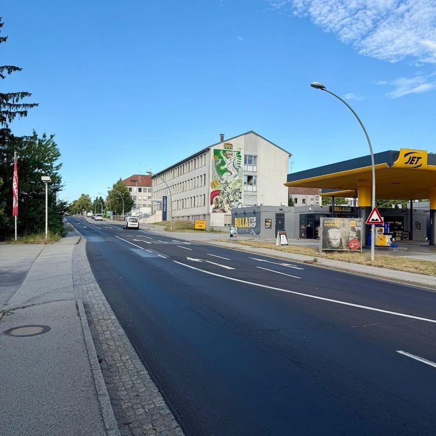 An empty street with a gas station on the right side. A mural is on the building, and a car is driving on the road.