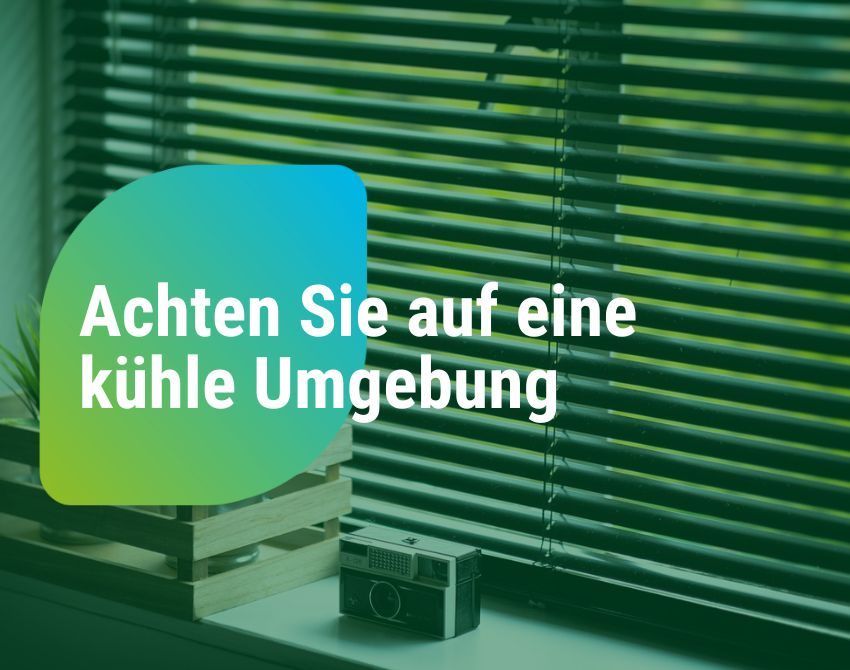 Ein Fenster mit Jalousien und einem grünen Schild, das 'Achten Sie auf eine kühle Umgebung' sagt, mit einer Vintage-Kamera auf der Fensterbank.