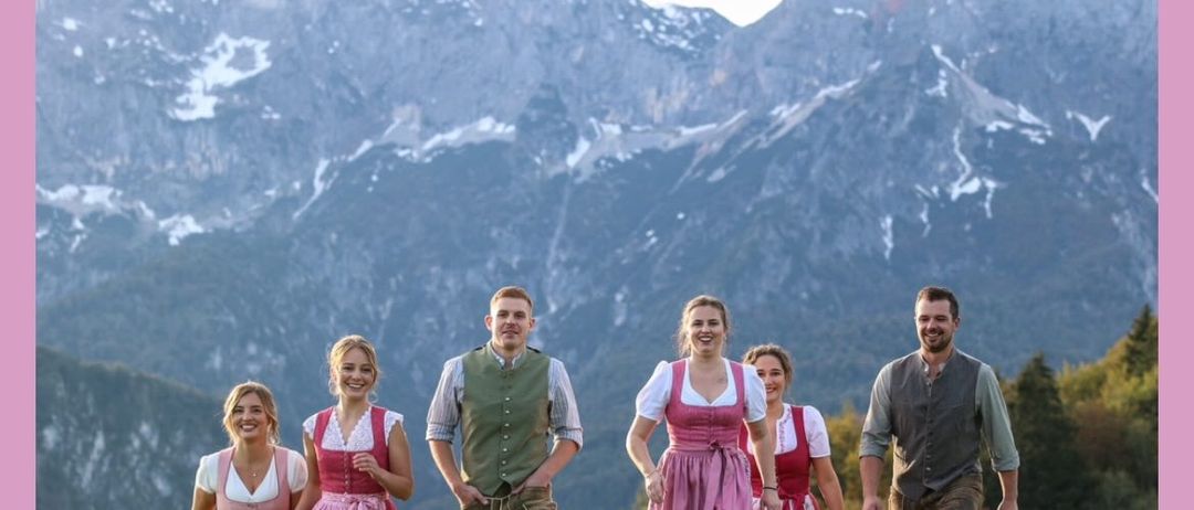 Eine Gruppe von Menschen in traditioneller Kleidung geht vor einer Berglandschaft über eine Wiese. Der Text überlagert 'Vieles bereits bis zu 50% reduziert!'. Das Bild trägt den Titel 'Ausgenommen orig.' auf Deutsch.