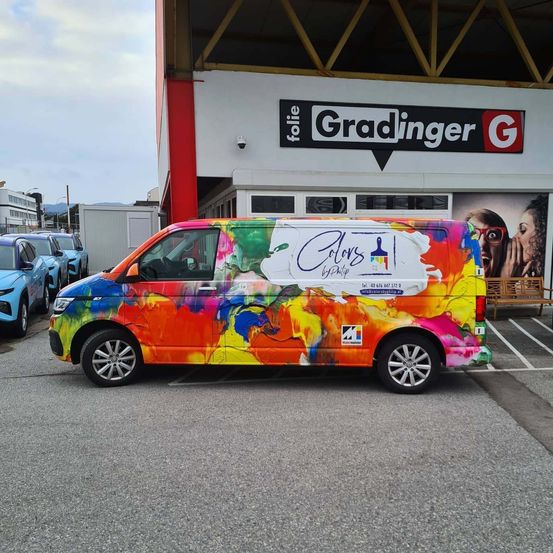Ein farbenfroher Van mit künstlerischen Designs ist auf einem Parkplatz vor einem Gebäude mit einem Schild für Folie Gradinger geparkt.