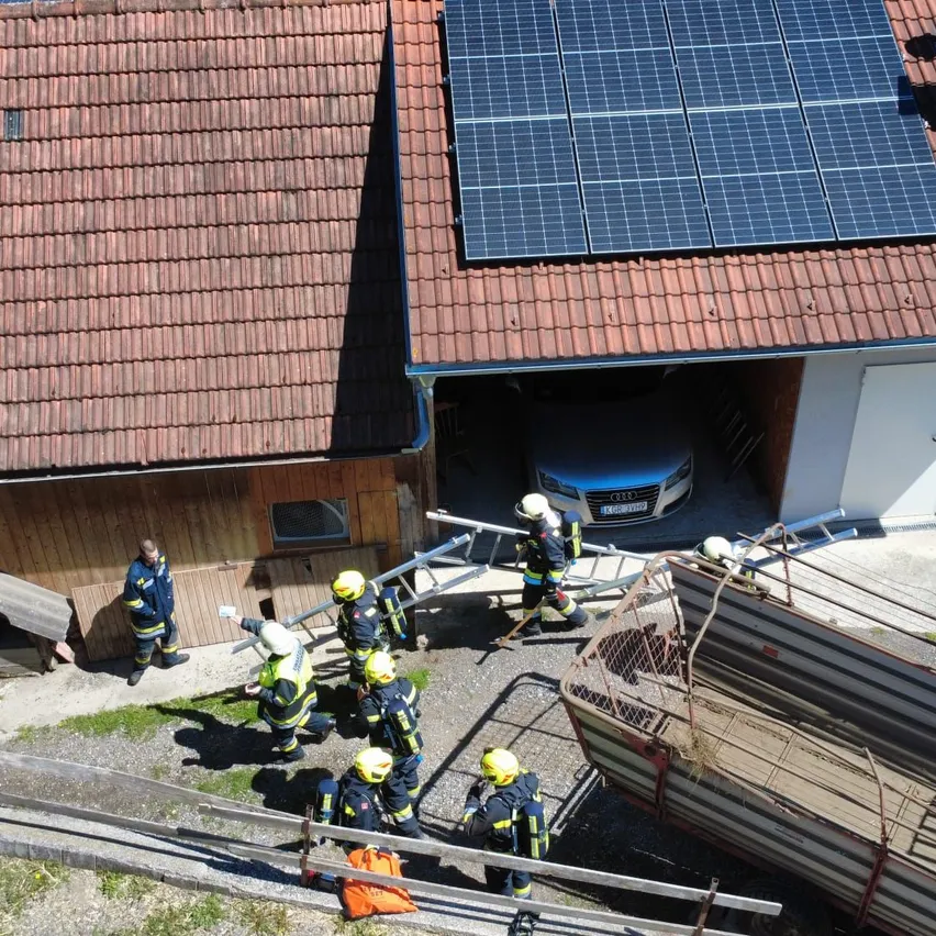 Eine Draufsicht von Feuerwehrleuten in gelben Helmen und Uniformen, die an einem Haus mit Solarmodulen auf dem Dach arbeiten.