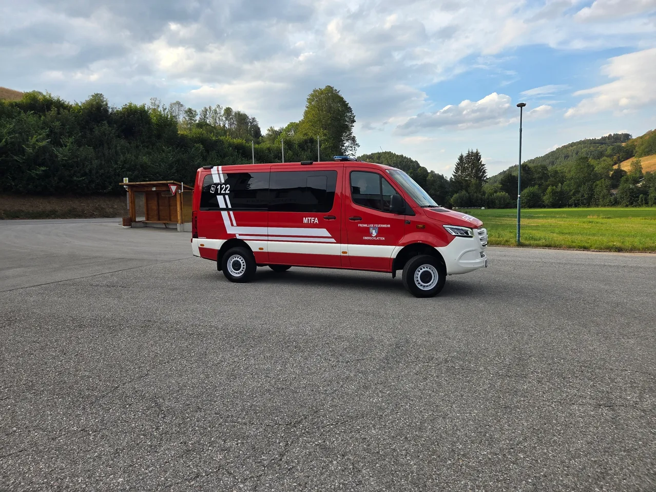 Ein rotes und weißes Notfallfahrzeug mit der Nummer 122 steht auf einem Parkplatz mit einem Rasenfeld und Bäumen im Hintergrund.