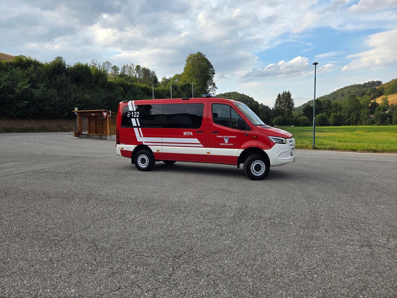 Ein rotes und weißes Notfallfahrzeug mit der Nummer 122 steht auf einem Parkplatz mit einem Rasenfeld und Bäumen im Hintergrund.
