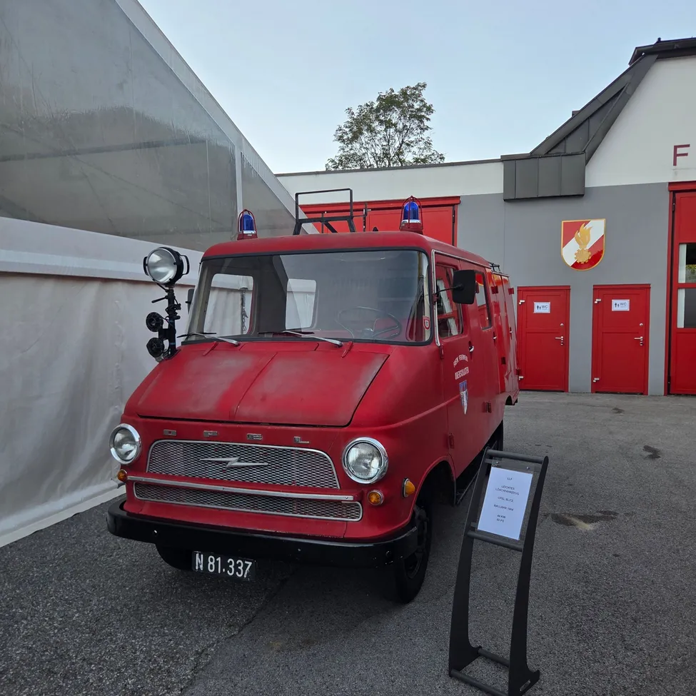Ein roter Vintage-Feuerwehrwagen steht vor einem Gebäude mit roten Türen. Der Wagen hat ein Nummernschild, das N 81.337 liest.