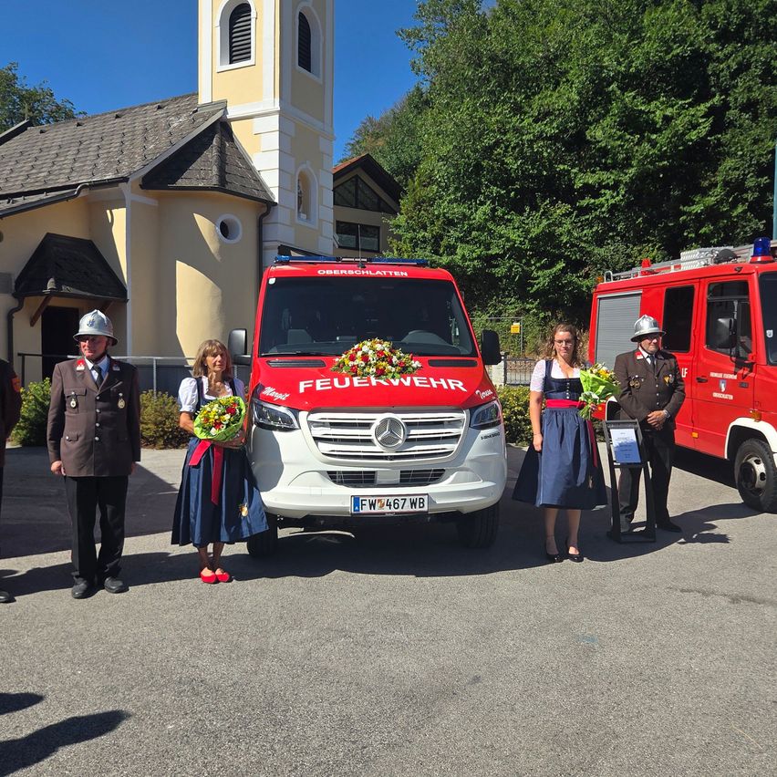 A group of people in traditional attire stand beside a red fire truck with flowers in front of a church.