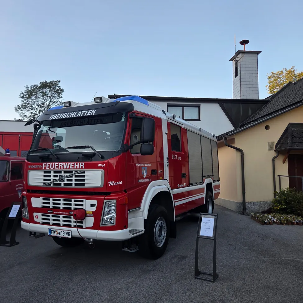 Ein roter Feuerwehrwagen mit der Aufschrift 'Feuerwehr' auf der Front ist vor einem Gebäude geparkt. Das Kennzeichen lautet 'FW 469 WB'.