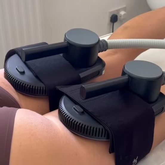 Eine Person liegt auf einem Bett mit schwarzen Riemen um die Beine, die mit einem Gerät verbunden sind. Die Riemen haben Knöpfe und das Gerät ist an einer Steckdose angeschlossen.