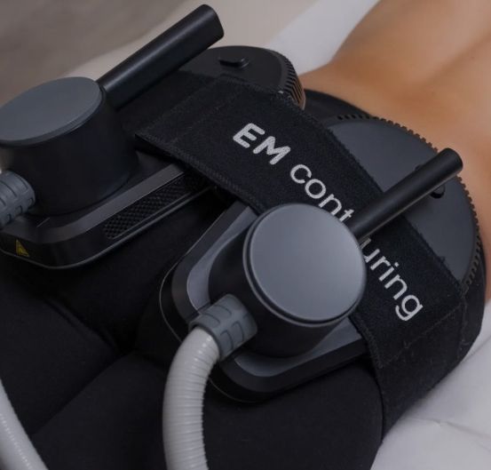 Eine Person trägt ein schwarzes EM-Konturierungsgerät mit einem angeschlossenen weißen Schlauch und liegt auf einem weißen Tuch.