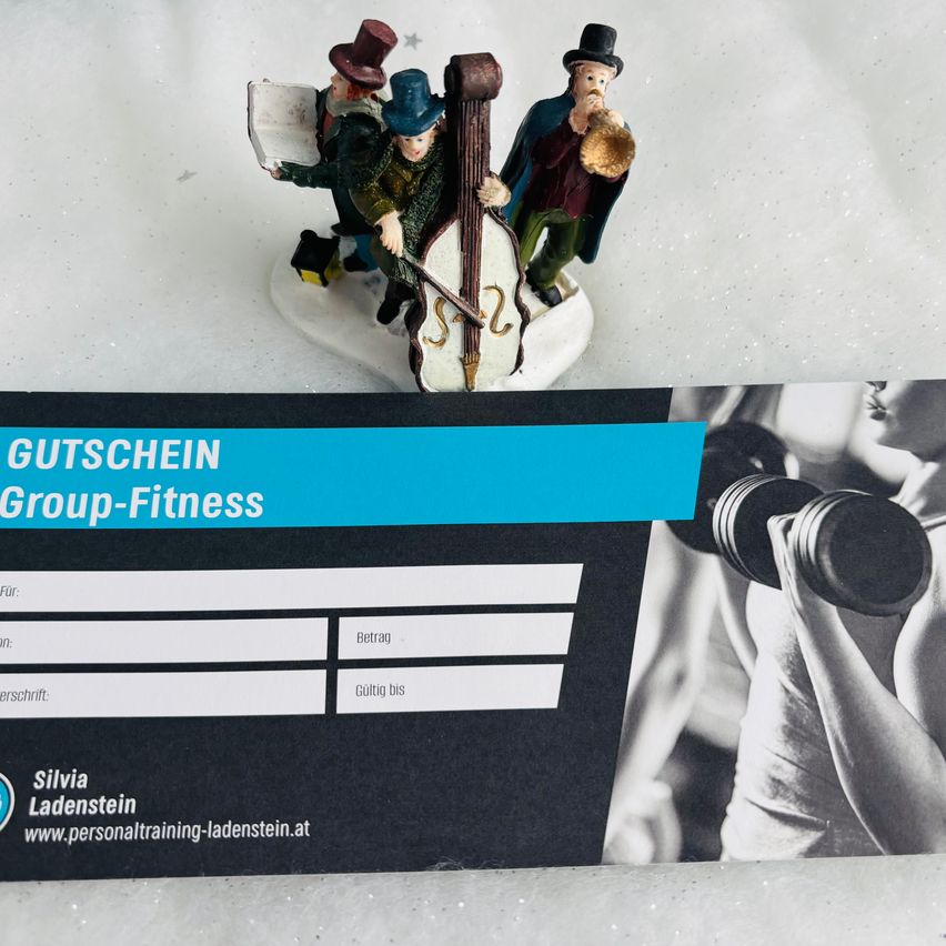 Ein Fitnessgutschein liegt auf einer weißen Oberfläche. Dahinter stellen drei Figuren Musiker dar. Der Gutschein ist blau und schwarz. Der Text sagt Gutschein Group-Fitness und Silvia Ladenstein. Auf der rechten Seite ist eine Hand zu sehen, die Hanteln hält.