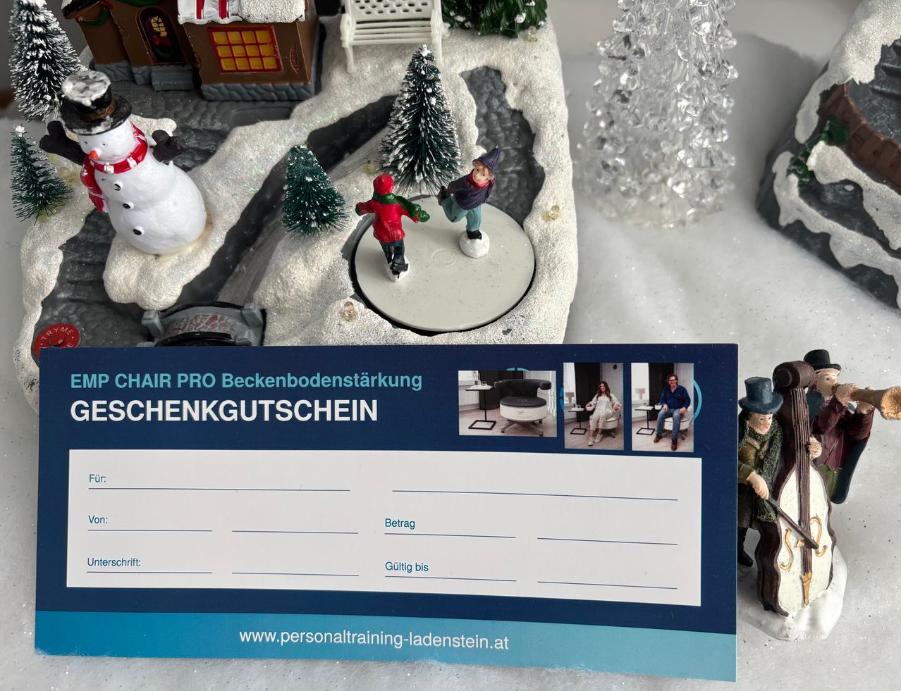 Eine weihnachtliche Szene zeigt einen verschneiten Bereich mit einem Miniatur-Schneemann, Miniaturfiguren und Miniaturbäumen. Ein Geschenkgutschein für 'Chair Pro Beckenbodenstarkung' ist prominent ausgestellt und enthält eine Website-Adresse.
