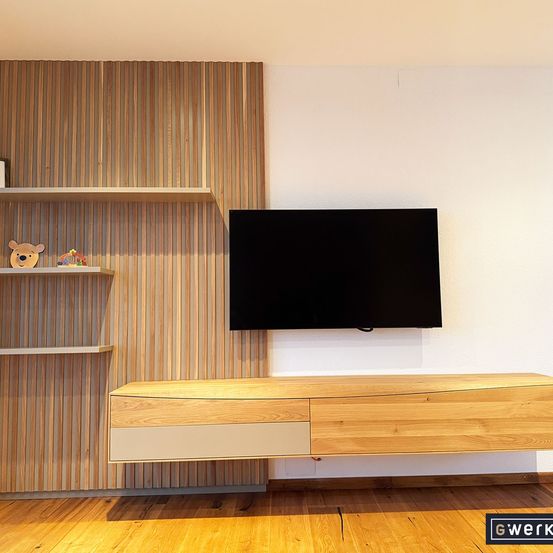 Ein modernes Zimmer mit Holzböden, Wänden und Möbeln. Ein Fernseher ist an der Wand über einem Holzregal mit einer Bärenfigur montiert.