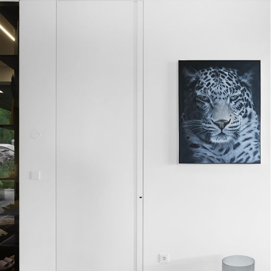 Eine weiße Wand mit einem montierten Foto eines Leoparden mit ernster Miene. Die Wand ist sauber und minimalistisch, ohne andere Dekorationen.
