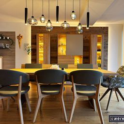 Ein moderner Essbereich mit einem Holztisch und Stühlen, Pendelleuchten und einer Holzwand mit Regalen und Schränken.