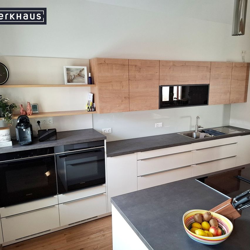 Eine moderne Küche mit weißen Schränken, Holzregalen, einer schwarzen Arbeitsplatte und einem Waschbecken mit Wasserhahn.