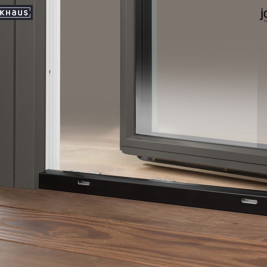 Ein Bild einer modernen Schiebetür mit Glasscheibe und grauem Rahmen. Die Tür ist geöffnet und zeigt einen Holzboden. Der Markenname 'jokhaus' ist auf der Tür sichtbar.