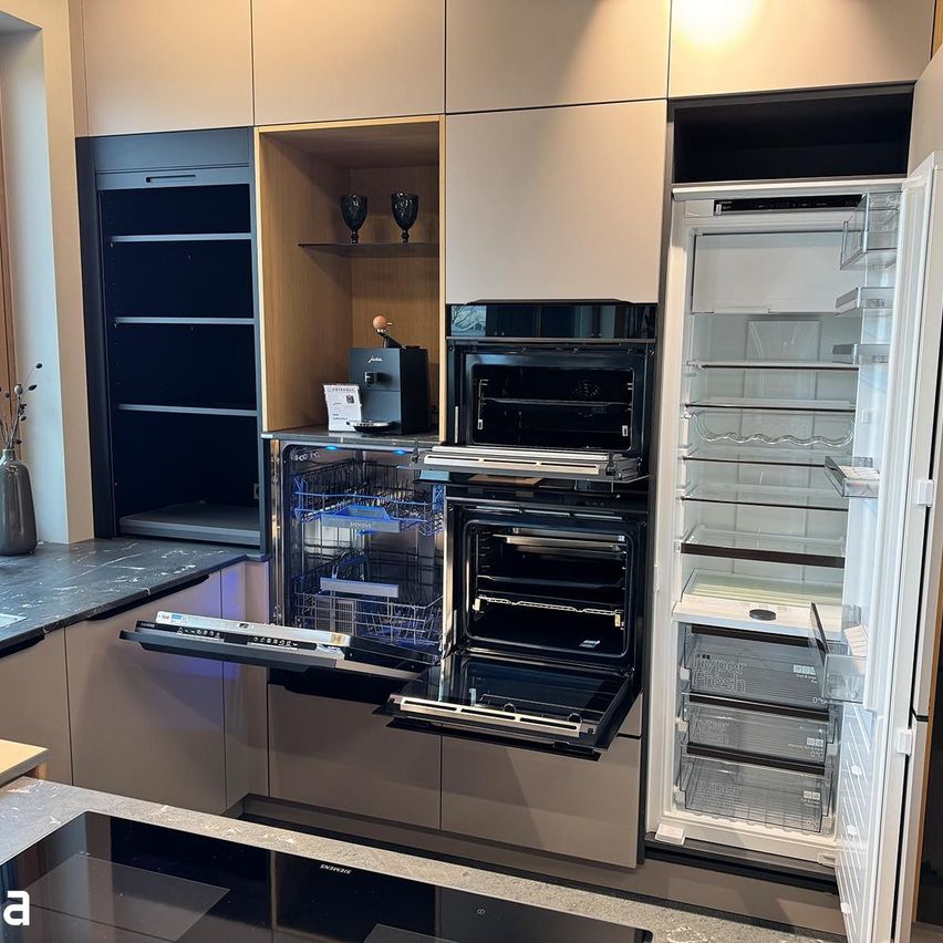 Modern kitchen with built-in appliances, including an open refrigerator, a dishwasher, and an oven, set against a backdrop of sleek cabinets and a countertop.