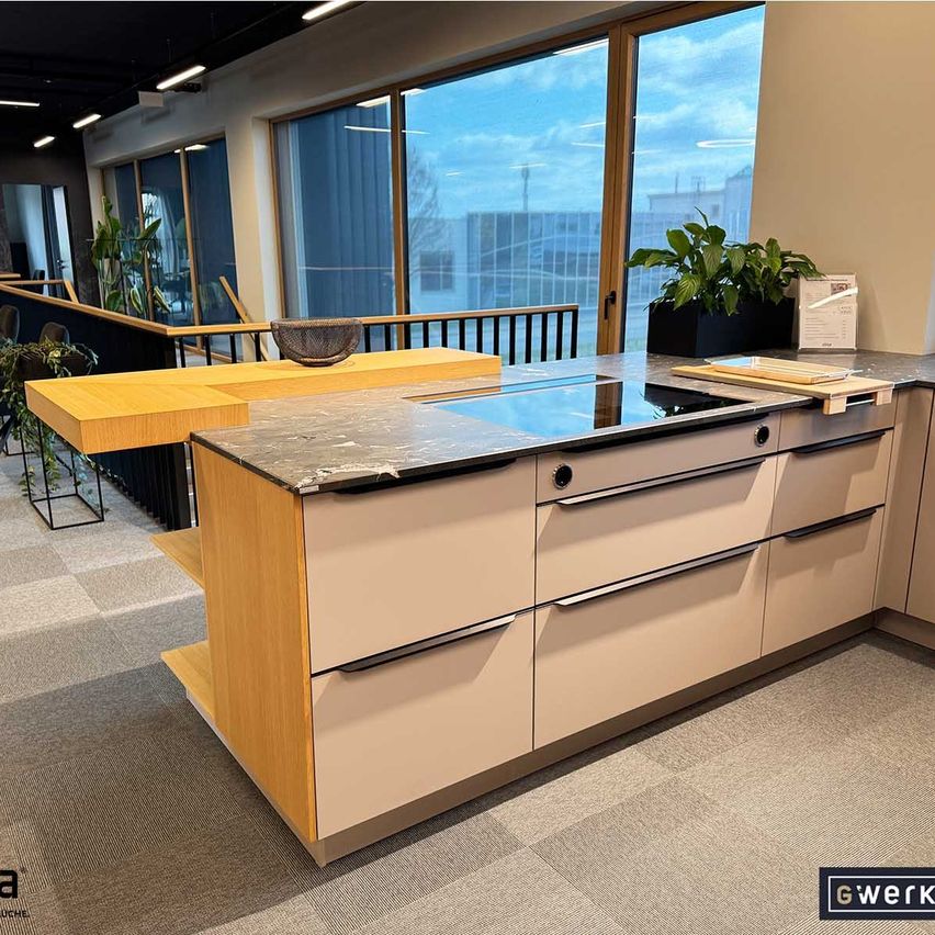 A modern kitchen with wooden cabinets and a granite countertop, featuring a gas stove and large windows with a view of a building.