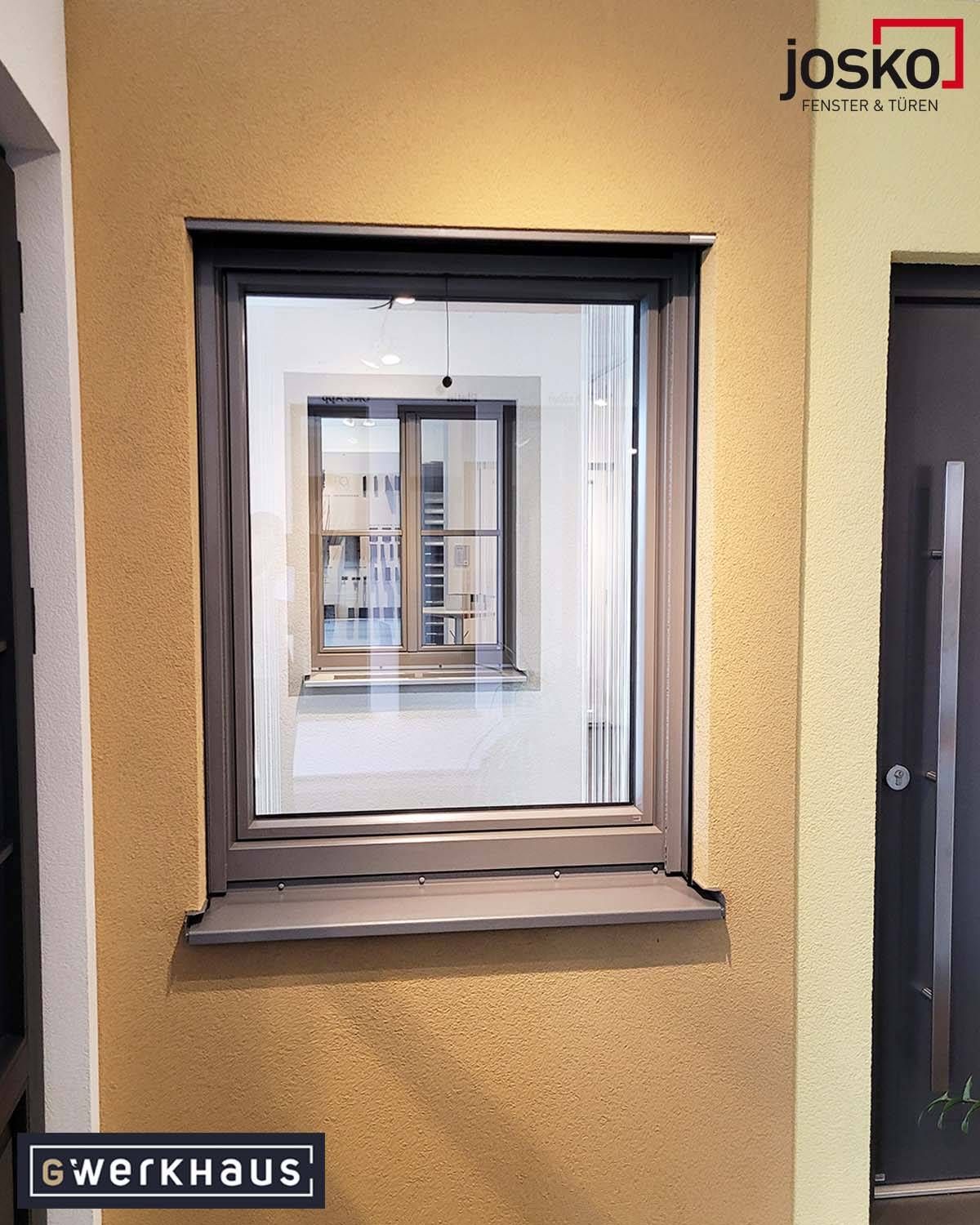 Ein modernes Fenster mit grauem Rahmen und Blick auf einen Balkon und ein weiteres Fenster auf der gegenüberliegenden Seite.
