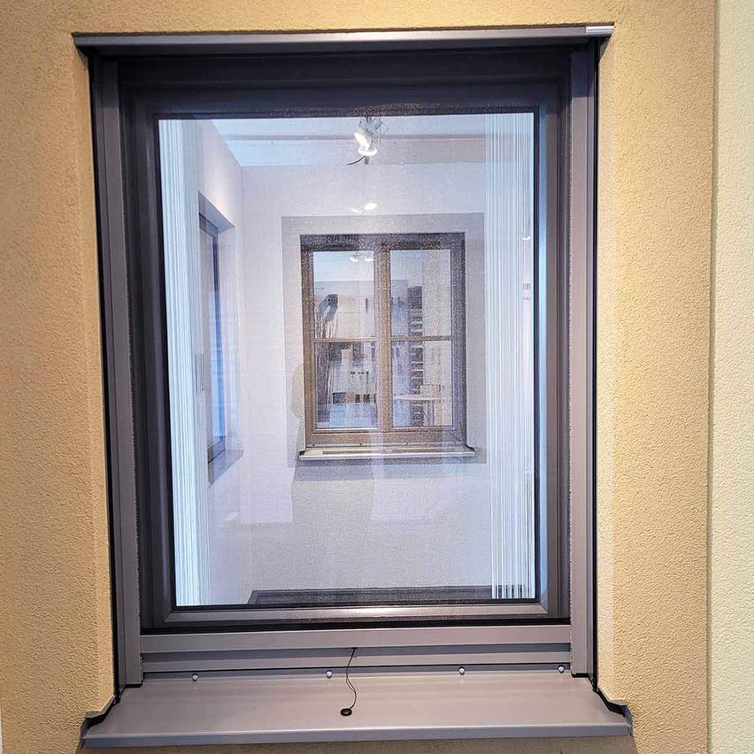 Ein Fenster mit schwarzem Rahmen und Glasscheibe, das die Reflexion eines Raumes mit einem Bilderrahmen und einem Fenster zeigt.