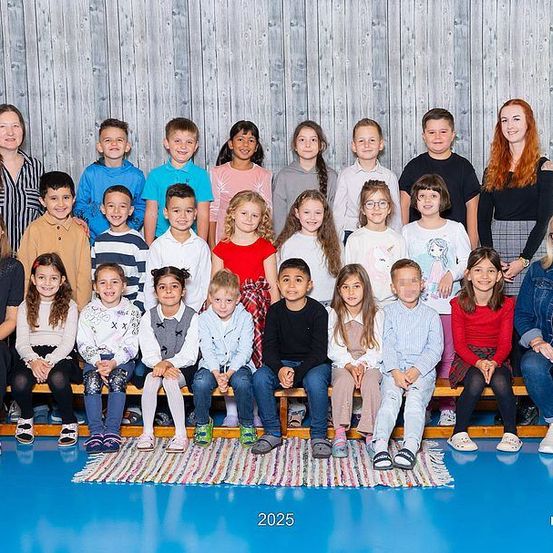 Eine Gruppe von Kindern und Lehrern, die in einer Turnhalle für ein Foto posiert. Das Jahr 2025 steht auf dem Boden.