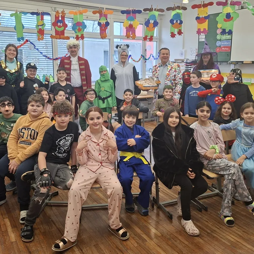 Eine Gruppe von Kindern und Erwachsenen in Kostümen posiert für ein Foto in einem Klassenzimmer mit festlichen Dekorationen.