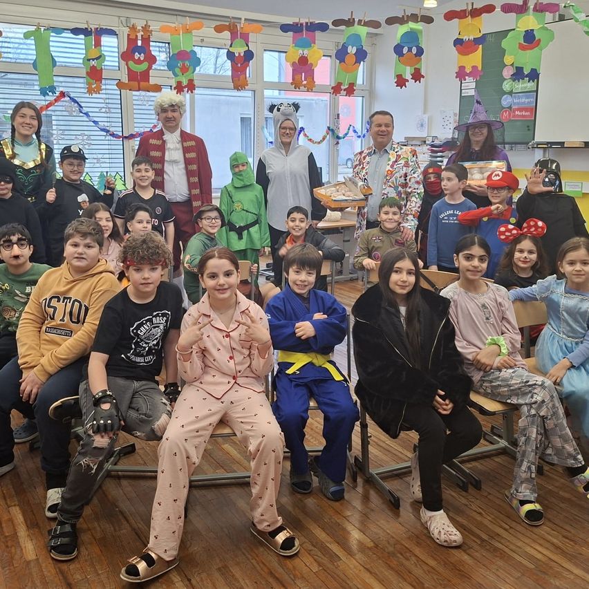 Eine Gruppe von Kindern und Erwachsenen in Kostümen posiert für ein Foto in einem Klassenzimmer mit festlichen Dekorationen.
