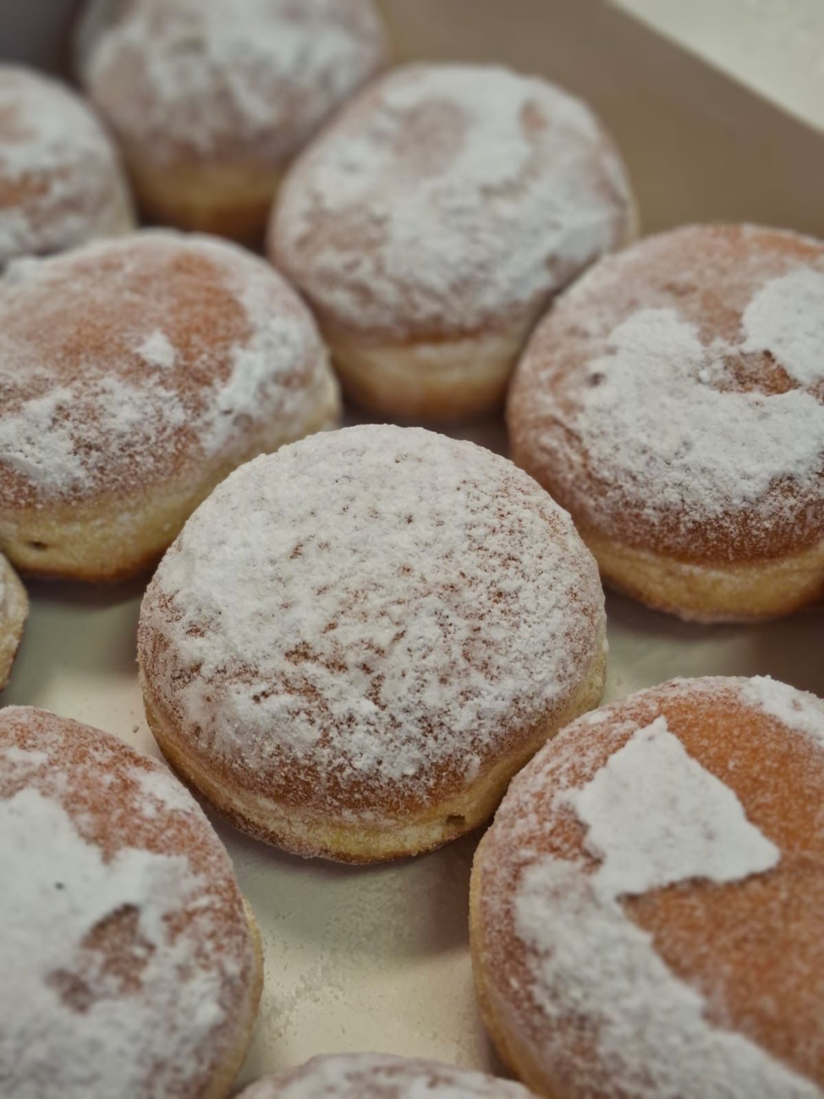 Eine Nahaufnahme von mehreren mit Puderzucker bedeckten Donuts auf einer weißen Oberfläche, einige mit Formen wie Herzen und Dreiecken.