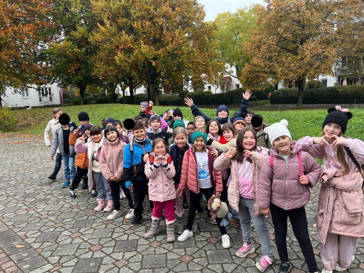 Eine Gruppe von Kindern, in Winterkleidung gekleidet, posiert für ein Foto in einem Park im Freien mit Herbstbäumen im Hintergrund.