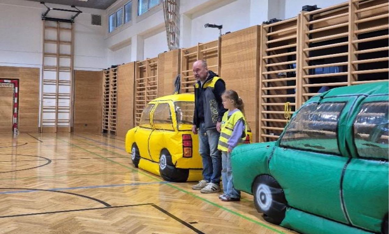 Ein Mann und ein Mädchen stehen neben aufblasbaren Autos in einer Turnhalle.