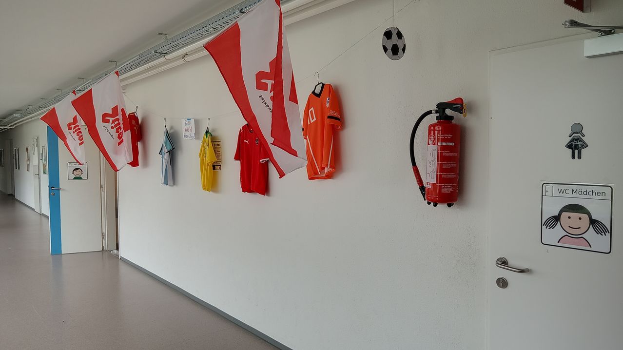 Ein Flur mit Trikots und einer Fahne an der Wand, ein Fußball über einem Feuerlöscher.