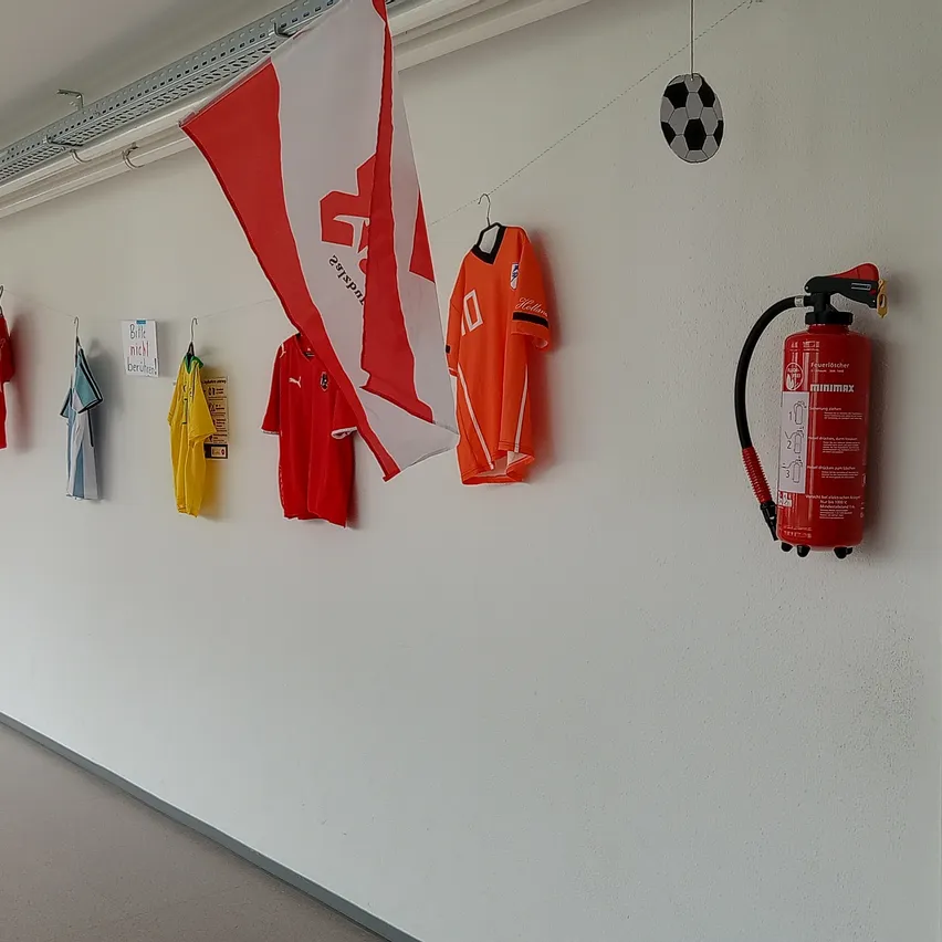 Ein Flur mit Trikots und einer Fahne an der Wand, ein Fußball über einem Feuerlöscher.