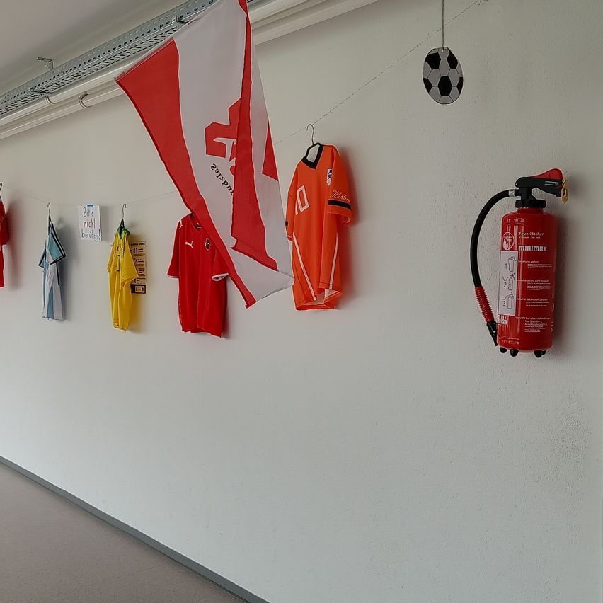 Ein Flur mit Trikots und einer Fahne an der Wand, ein Fußball über einem Feuerlöscher.