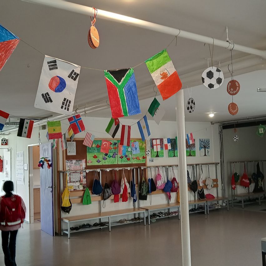 Ein Klassenzimmer mit verschiedenen Flaggen und Zeichnungen dekoriert. Ein Schüler geht durch den Eingang.