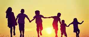 Fünf Kinder laufen Hand in Hand auf einem Feld mit dem untergehenden Sonnen im Hintergrund.