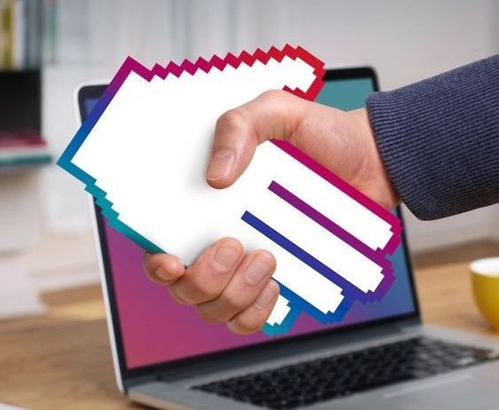 Eine Person gibt einem pixeligen Symbol auf einem Laptop-Bildschirm die Hand, mit einem Bücherregal im Hintergrund.