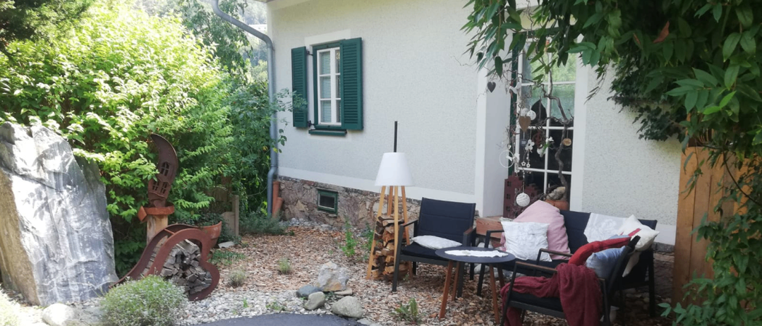Ein weißes Haus mit grünen Fensterläden und einem Garten mit Tisch und Stühlen.